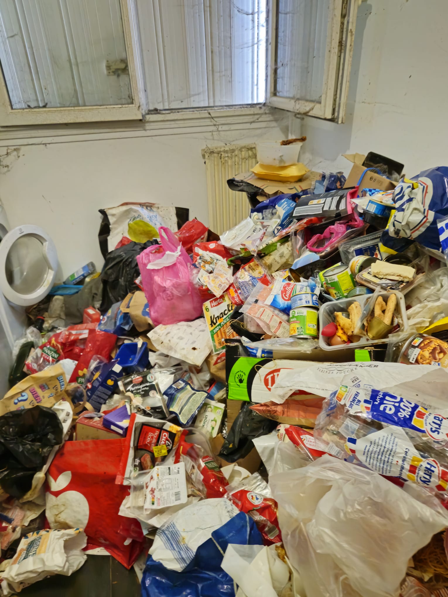 Pièce avec accumulation massive de déchets alimentaires devant un radiateur — risque sanitaire et nuisibles