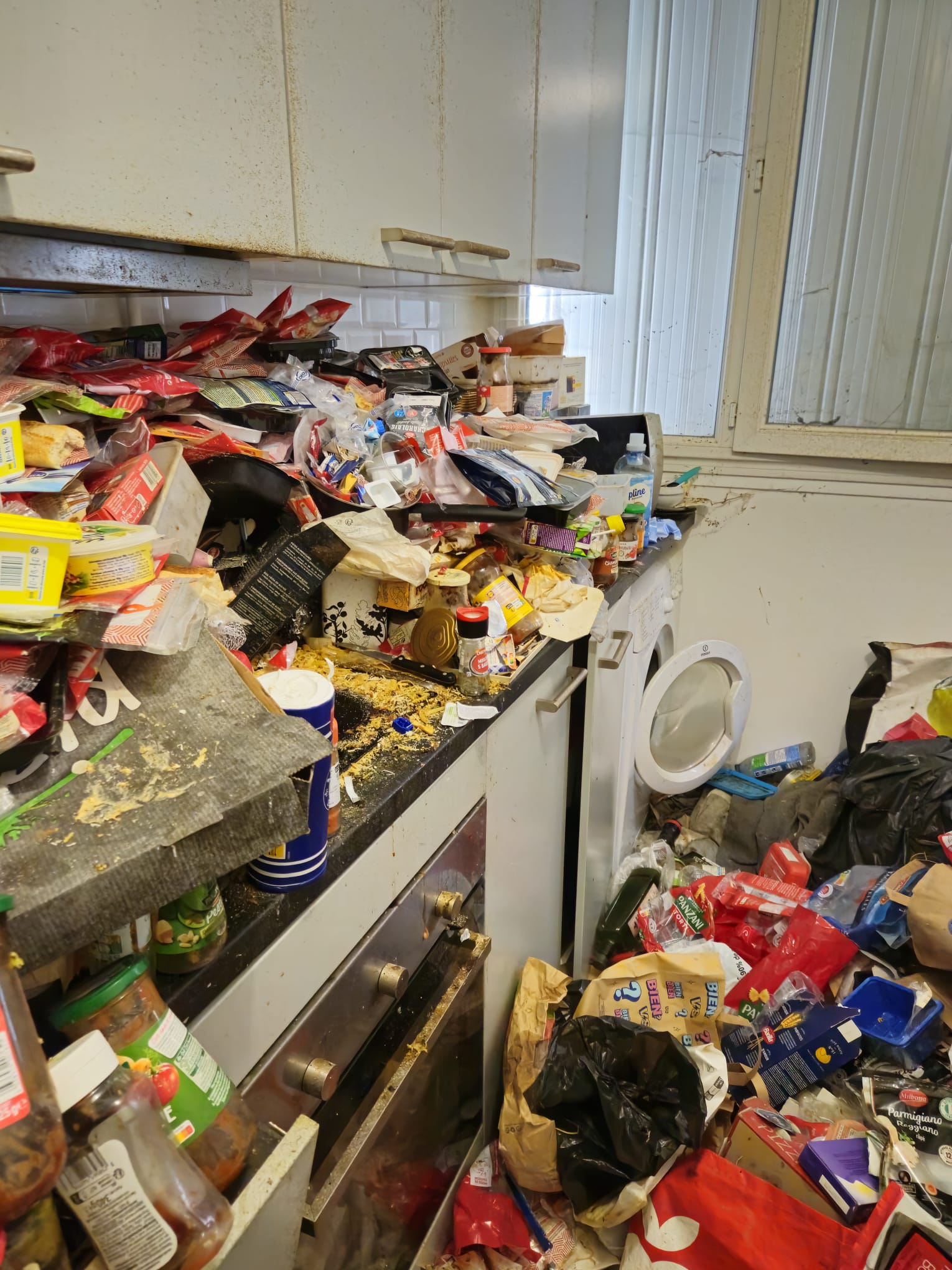 Cuisine avec amas de bocaux de sauces tomates, d'huiles et de sacs plastique, plan de travail saturé