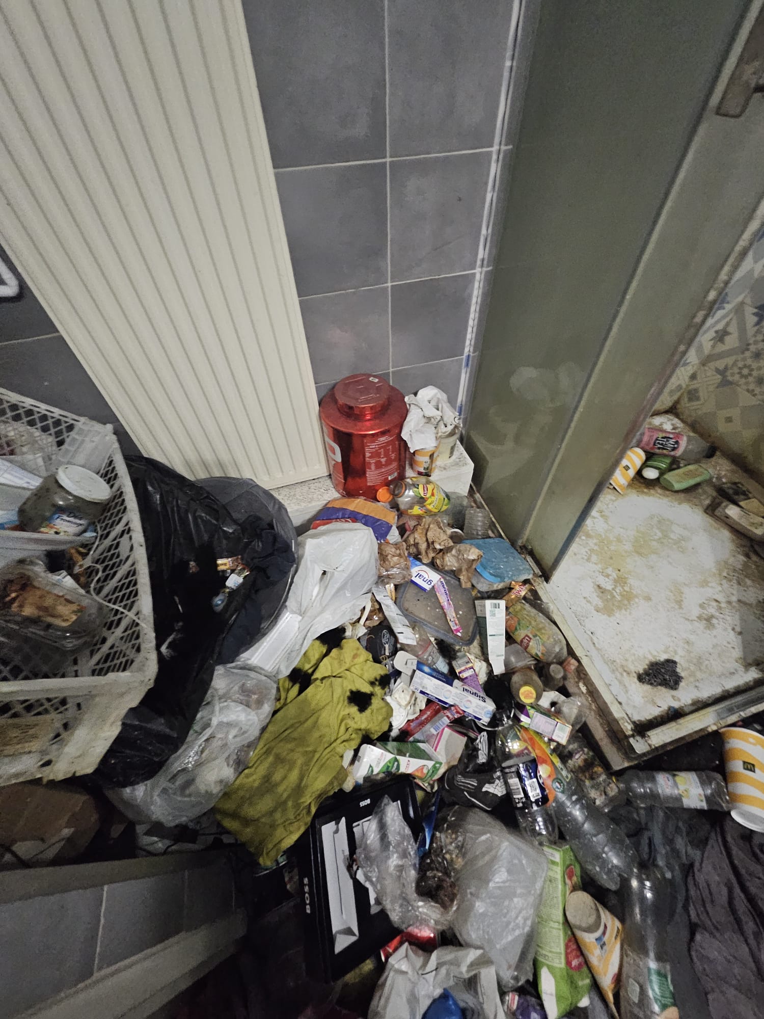 Salle de bains avec déchets et bouteilles au sol, autour de la douche, contamination généralisée